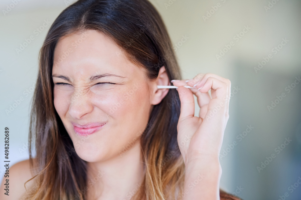 That tickles. Shot of young woman pulling a funny face while cleaning her ear with an earbud at home. That tickles. Shot of young woman pulling a funny face while cleaning her ear with an earbud at home.