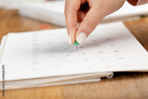 a female hand with a beautiful manicure holds a green pushpin to mark the date on the calendar