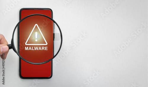 Fotografia Magnifying glass on cell phone, an alarm sign detecting malware