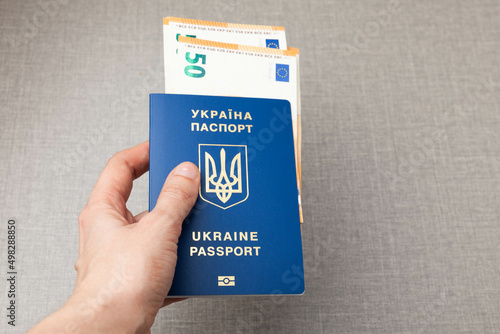 Hand holding Ukrainian passport with european money euro on gray table background. Refugees protection concept. photo