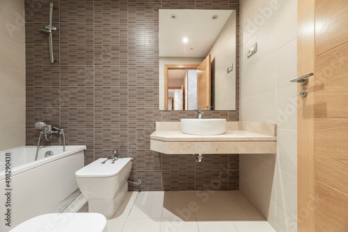 Bathroom with wooden cabinets  white porcelain sink on marble countertop  brown tiles and frameless mirror