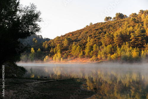 Morning fog over the still lake with water mirror at sunrise