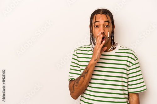 Young African American man isolated on white background is saying a secret hot braking news and looking aside