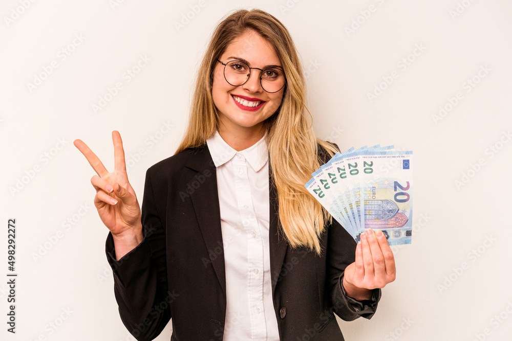 Young business caucasian woman holding a banknotes isolated on white background joyful and carefree showing a peace symbol with fingers. Young business caucasian woman holding a banknotes isolated on white background joyful and carefree showing a peace symbol with fingers.
