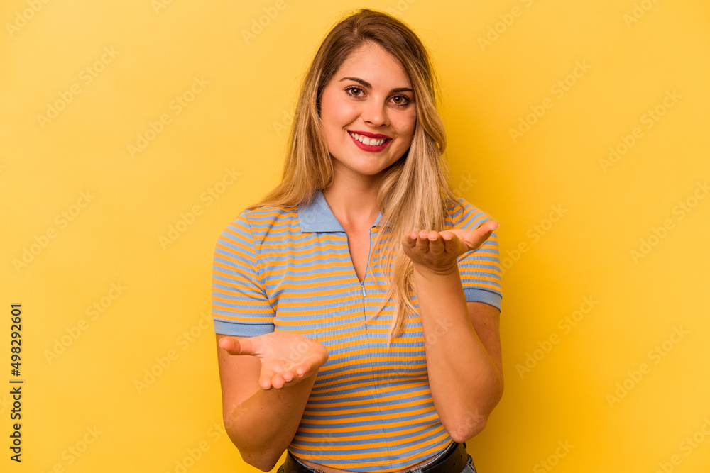 Young caucasian woman isolated on yellow background makes scale with arms, feels happy and confident. Young caucasian woman isolated on yellow background makes scale with arms, feels happy and confident.