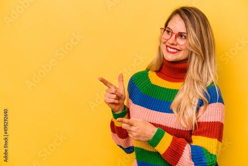 Young caucasian woman isolated on yellow background points with thumb finger away  laughing and carefree.