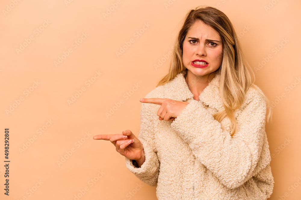 Young caucasian woman isolated on beige background shocked pointing with index fingers to a copy space.