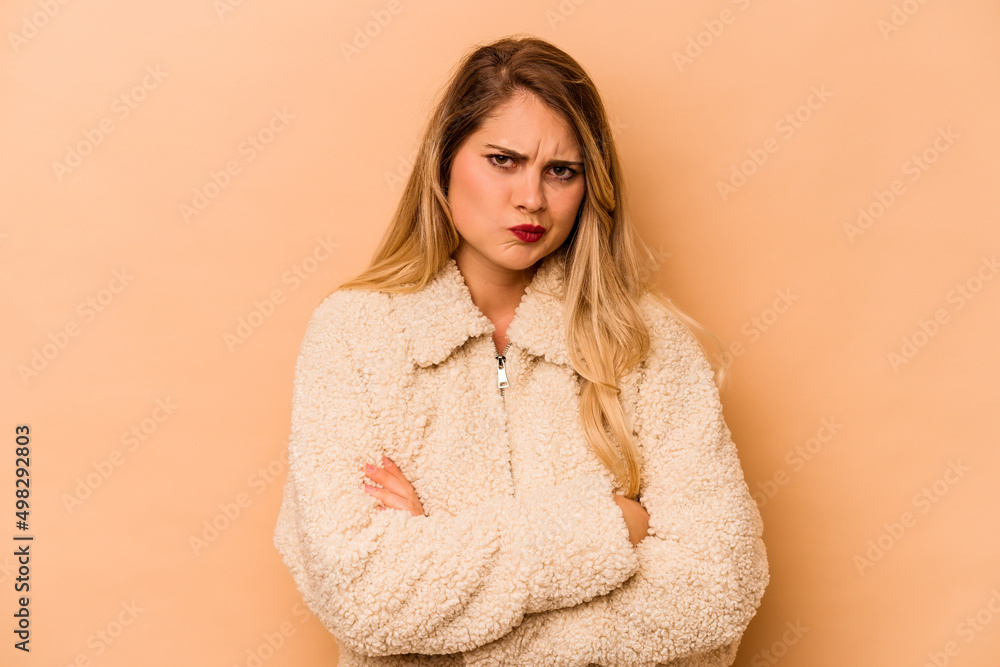 Young caucasian woman isolated on beige background frowning face in displeasure, keeps arms folded. Young caucasian woman isolated on beige background frowning face in displeasure, keeps arms folded.