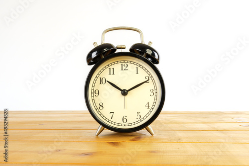 Black retro alarm clock put on wooden table isolated on white background.