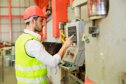 lathe and stamping metal machine. Hispanic man and Factory engineer in hard hat helmet working on digital teblet computer at Heavy Industry Manufacturing Factory.