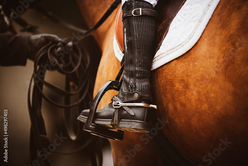 The chestnut horse is wearing horse ammunition - a stirrup, a brown old saddle, a white saddlecloth, a bridle, and a rider in black boots is sitting in the saddle. Horse riding. Equestrian sports.