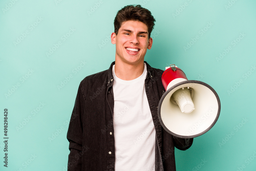 Young caucasian man holding a megaphone isolated on white background happy, smiling and cheerful. Young caucasian man holding a megaphone isolated on white background happy, smiling and cheerful.