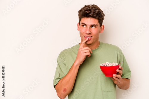 Young caucasian man eating cereals isolated on white background relaxed thinking about something looking at a copy space.