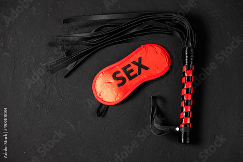 BDSM, bondage play, fetish wear and kinky sex toy concept with close up on erotic mask and red handcuffs isolated on black silk background
