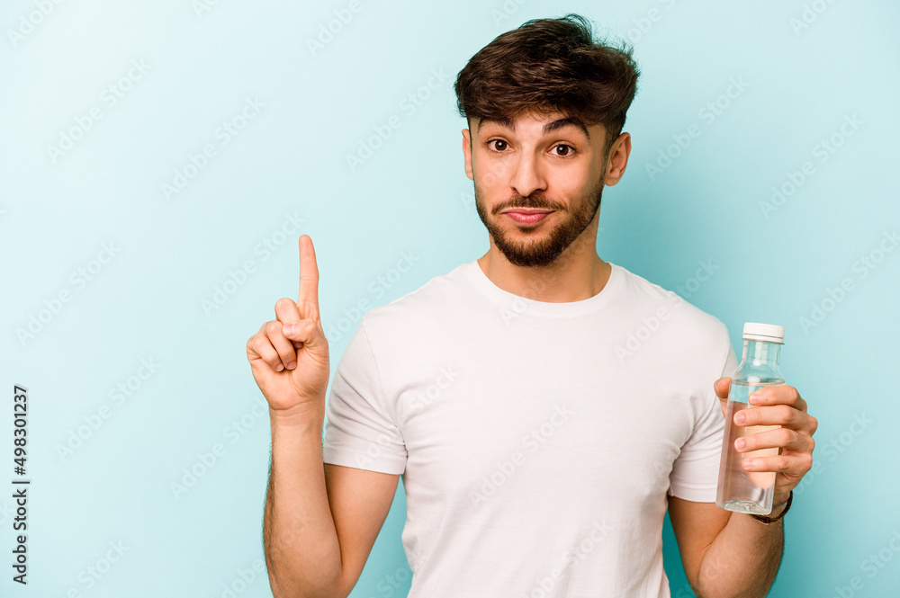 Young hispanic man holding a bottle of water isolated on white background showing number one with finger. Young hispanic man holding a bottle of water isolated on white background showing number one with finger.
