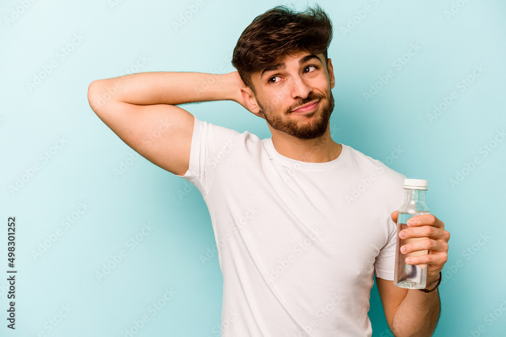 Young hispanic man holding a bottle of water isolated on white background touching back of head, thinking and making a choice. Young hispanic man holding a bottle of water isolated on white background touching back of head, thinking and making a choice.