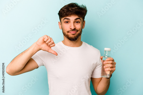 Young hispanic man holding a bottle of water isolated on white background showing a dislike gesture, thumbs down. Disagreement concept. © Asier