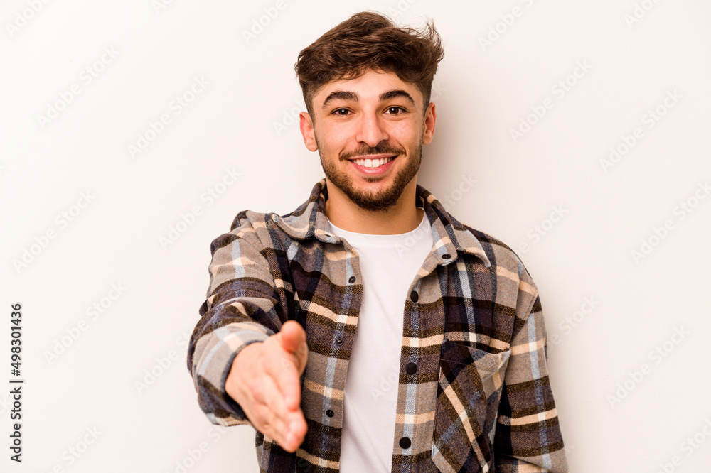 Young hispanic man isolated on white background stretching hand at camera in greeting gesture. Young hispanic man isolated on white background stretching hand at camera in greeting gesture.