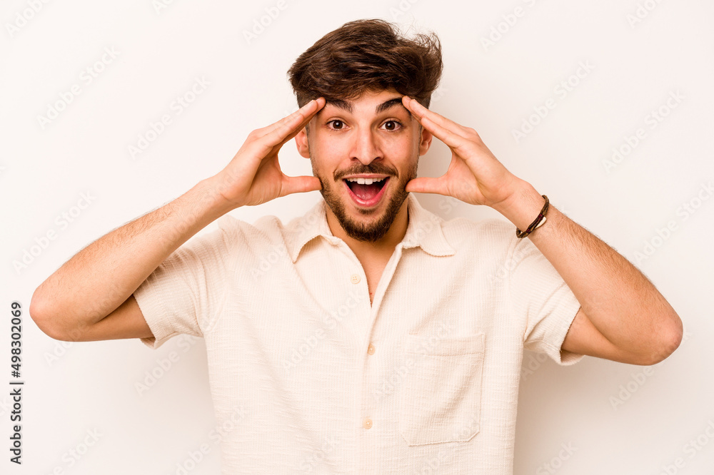 Naklejka premium Young hispanic man isolated on white background receiving a pleasant surprise, excited and raising hands.