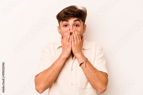 Young hispanic man isolated on white background shocked, covering mouth with hands, anxious to discover something new.