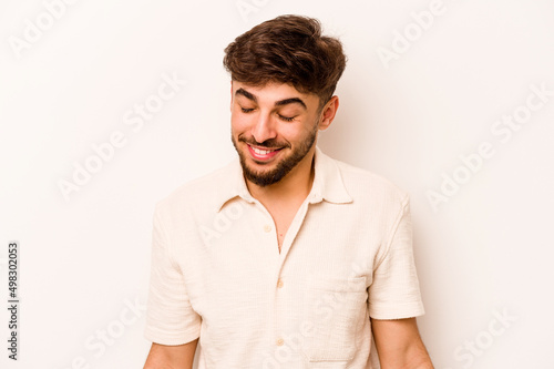 Young hispanic man isolated on white background laughs and closes eyes, feels relaxed and happy. © Asier