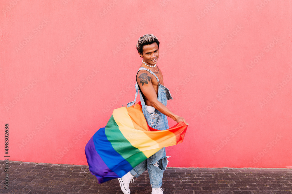 Smiling handsome guy walking outdoors with LGBT flag against pink wall