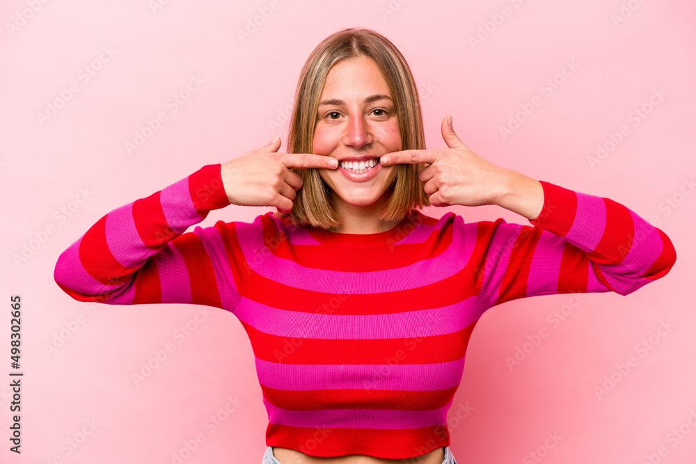 Young caucasian woman isolated on pink background smiles, pointing fingers at mouth. Young caucasian woman isolated on pink background smiles, pointing fingers at mouth.