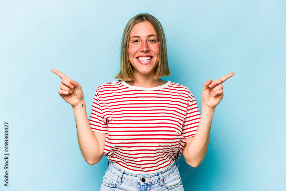 Young caucasian woman isolated on blue background pointing to different copy spaces, choosing one of them, showing with finger. Young caucasian woman isolated on blue background pointing to different copy spaces, choosing one of them, showing with finger.