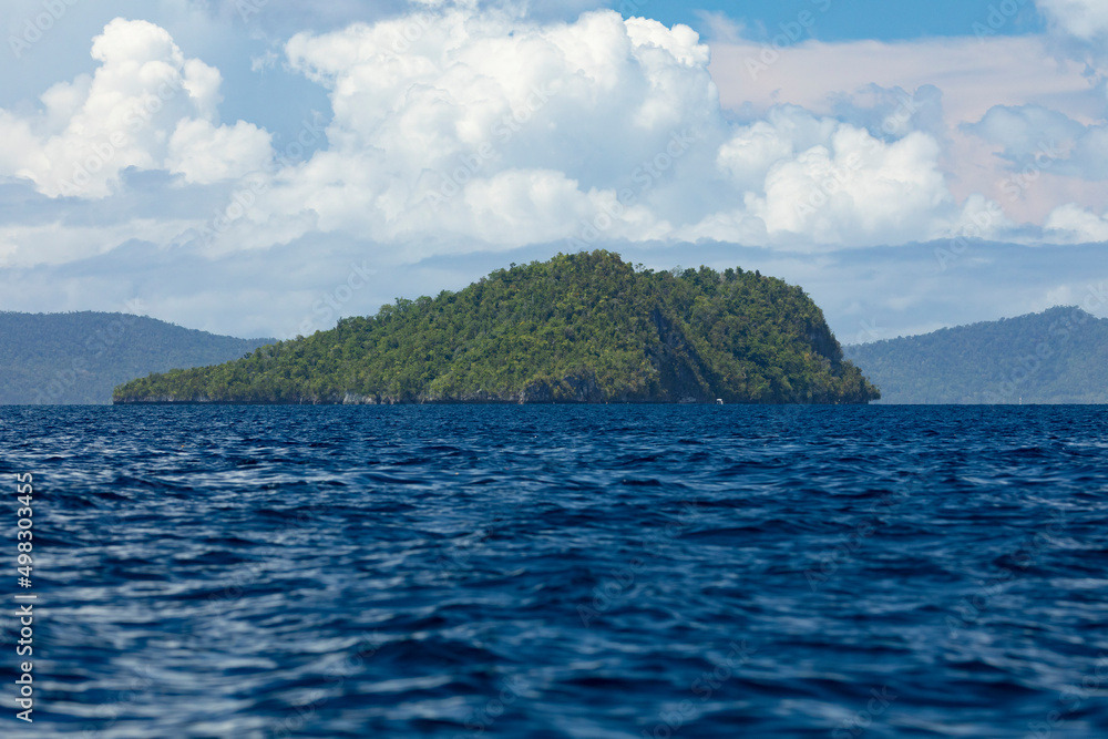 Dark water seascape, and a distant tropical island, in Raja Ampat islands, West papua, covered with jungle, Indonesia