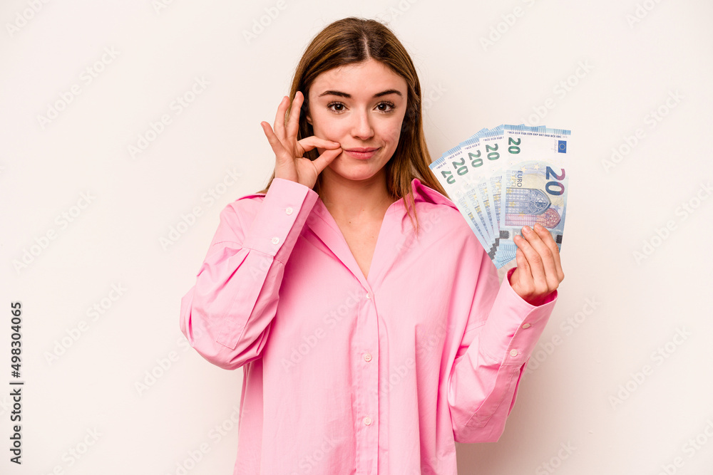 Young woman holding banknotes isolated on white background with fingers on lips keeping a secret. Young woman holding banknotes isolated on white background with fingers on lips keeping a secret.