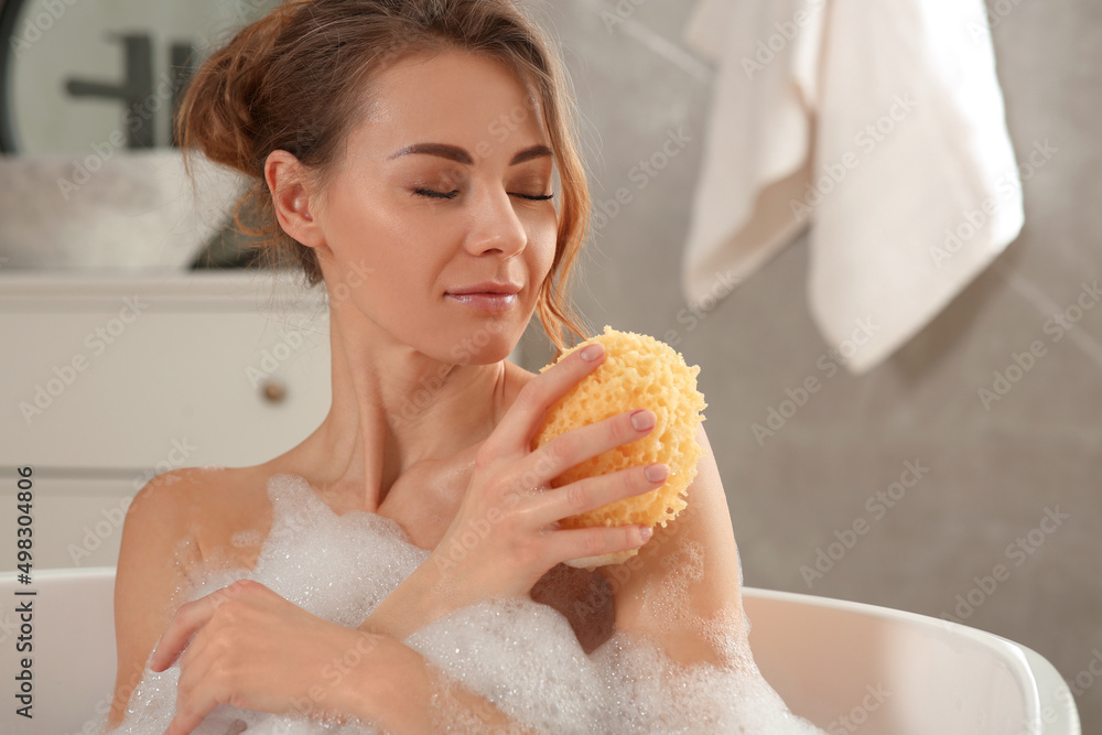 Beautiful woman with sponge taking bath indoors Beautiful woman with sponge taking bath indoors