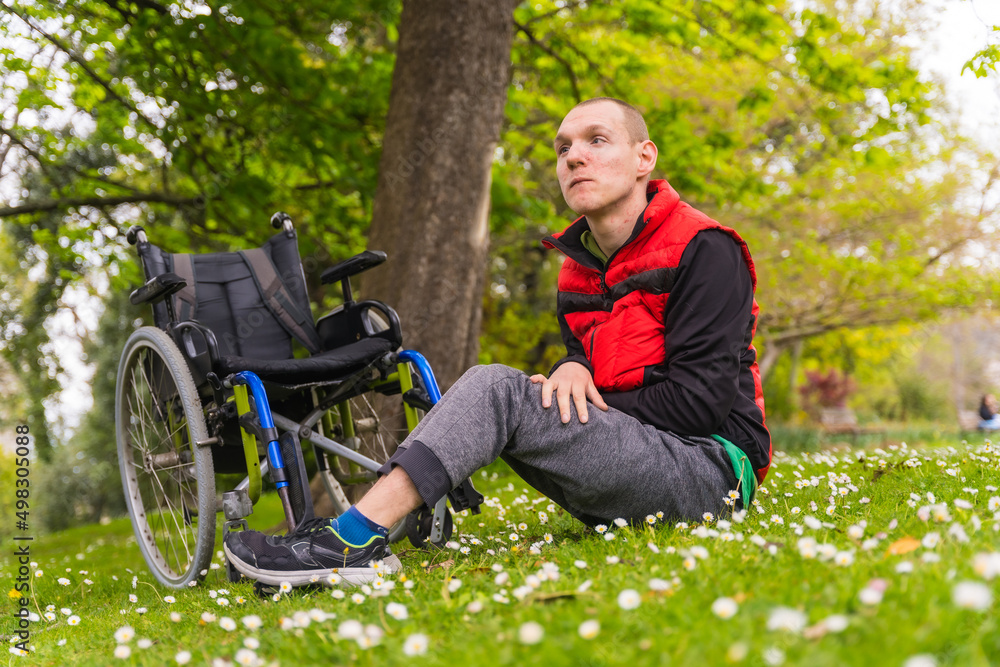 Portrait of a person with a disability sitting on the grass next to the wheelchair smiling, in the spring in a nature park Portrait of a person with a disability sitting on the grass next to the wheelchair smiling, in the spring in a nature park