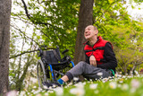 Portrait of a person with a disability sitting on the grass next to the wheelchair in a daisy flower, smiling and enjoying nature