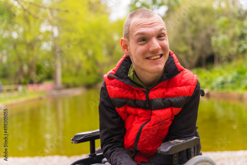 Portrait of a person with a disability in a public park in the city. Sitting in the wheelchair smiling looking at camera © unai