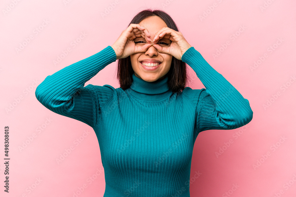 Young hispanic woman isolated on pink background showing okay sign over eyes Young hispanic woman isolated on pink background showing okay sign over eyes