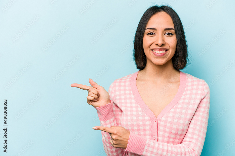 Young hispanic woman isolated on blue background excited pointing with forefingers away. Young hispanic woman isolated on blue background excited pointing with forefingers away.