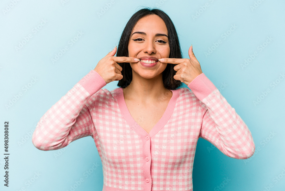 Young hispanic woman isolated on blue background smiles, pointing fingers at mouth. Young hispanic woman isolated on blue background smiles, pointing fingers at mouth.