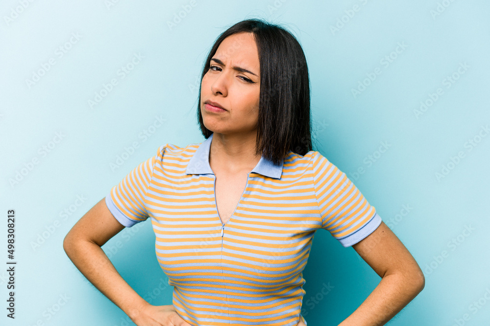 Obraz premium Young hispanic woman isolated on blue background frowning face in displeasure, keeps arms folded.