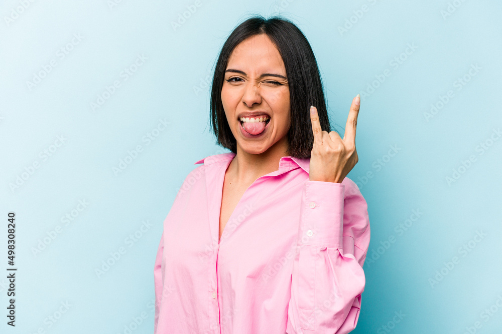 Young hispanic woman isolated on blue background showing rock gesture with fingers Young hispanic woman isolated on blue background showing rock gesture with fingers
