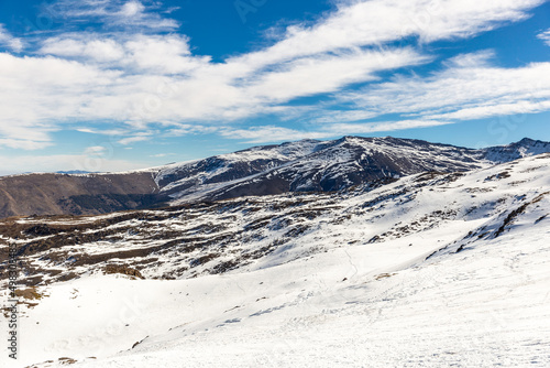 View of Sierra Nevada, Granada, Andalusia, Spain. Snow-capped mountains, sunny day. Ski runs and chairlift. Winter landscape with snow. 