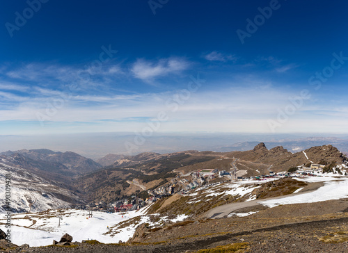 View of Sierra Nevada, Granada, Andalusia, Spain. Snow-capped mountains, sunny day. Ski runs and chairlift. Winter landscape with snow. View of the city