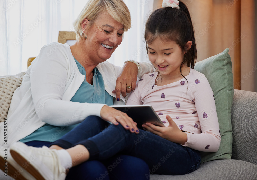 Let me see your score.... Shot of an adorable little girl using a digital tablet while sitting at home with her grandmother. Let me see your score.... Shot of an adorable little girl using a digital tablet while sitting at home with her grandmother.