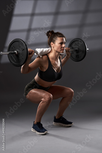 Fitness woman doing barbell squats with heavy discs