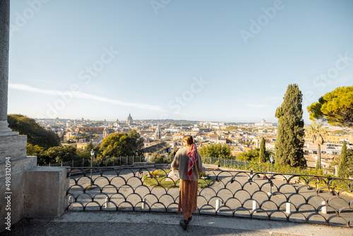 Woman enjoying beautiful morning cityscape of Rome, walking in Villa Borghese Park. Old fashioned woman wearing coat with colorful shawl in hair. Concept of italian lifestyle and travel