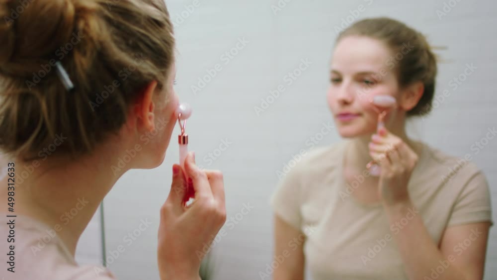 Beautiful lady in the bathroom looking in the mirror and using a face roller make some massage on her face carefully. 4k Beautiful lady in the bathroom looking in the mirror and using a face roller make some massage on her face carefully. 4k