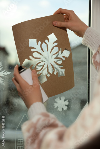 Obraz na plátně Woman using snow spray for decorating window with snowflakes at home, closeup