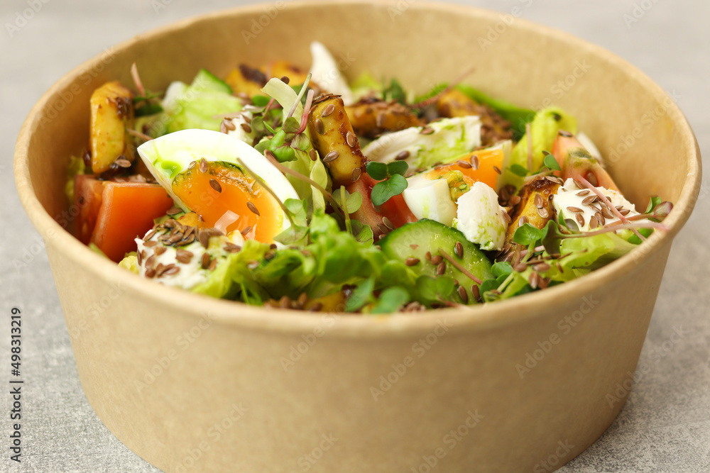 Healthy bowl with fried squid, egg, tomatoes, cucumbers, lettuce, cream cheese and flax seeds salad isolated on gray background. Food delivery service and daily ration concept. Healthy bowl with fried squid, egg, tomatoes, cucumbers, lettuce, cream cheese and flax seeds salad isolated on gray background. Food delivery service and daily ration concept.
