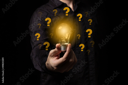 Question marks on a black background, searching for a solution in an unknown situation. Man holding a light bulb in his hand, idea of creativity and inspiration concept of sustainable business develop