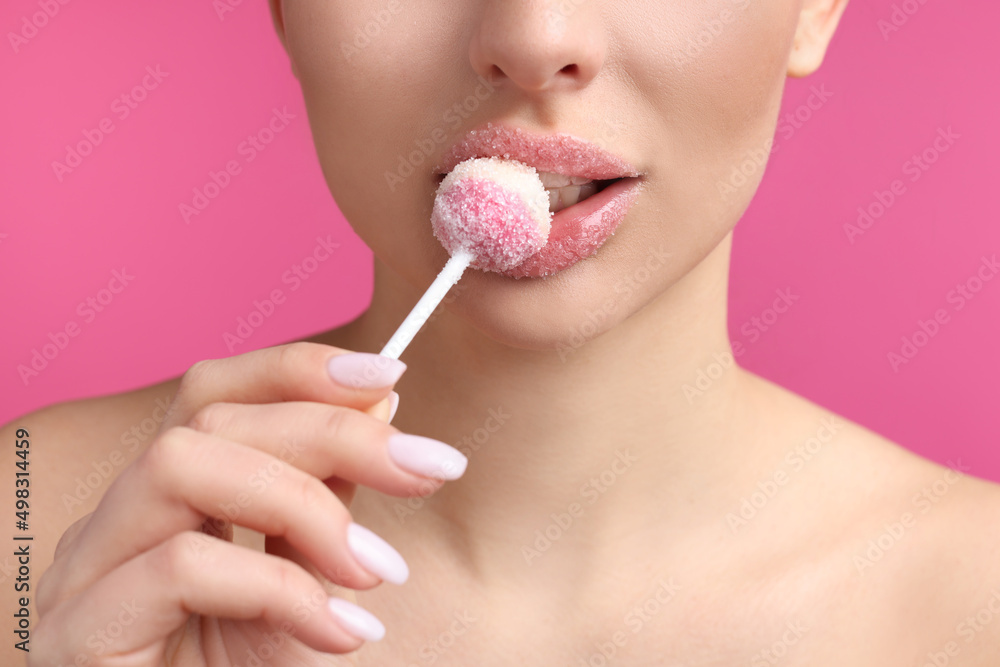 Young woman with beautiful lips covered in sugar eating lollipop on pink background, closeup Young woman with beautiful lips covered in sugar eating lollipop on pink background, closeup