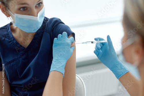wonan doctor or nurse giving shot or vaccine to patient shoulder. Vaccination and prevention against flu or virus pandemic. Covid-19 or coronavirus vaccine
